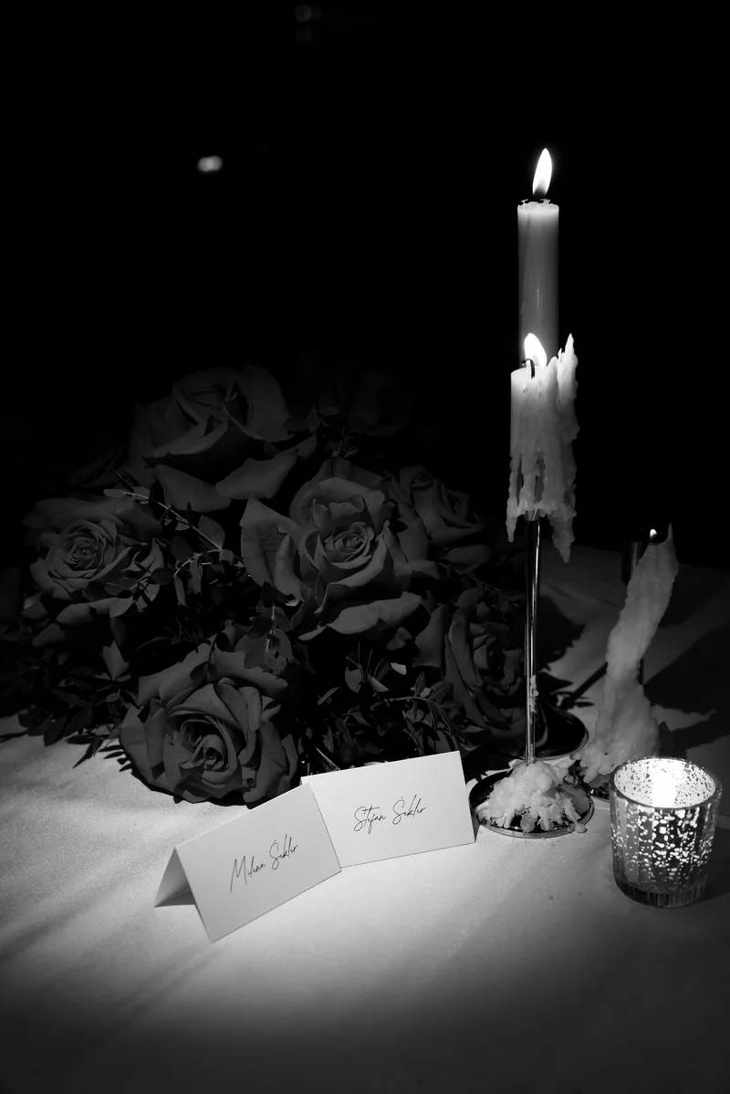 In black and white, handwritten place cards rest beside roses and a dripping taper candle in a silver holder.