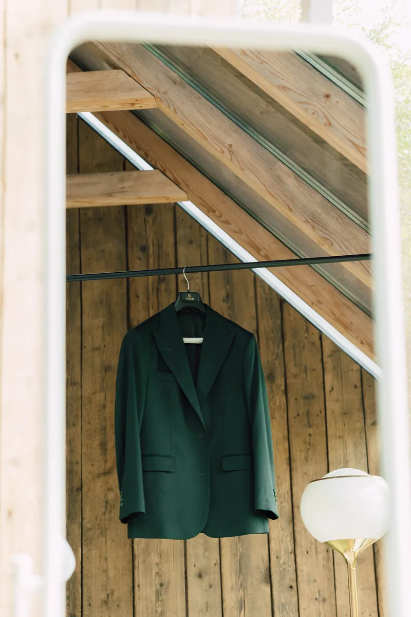 Emerald green suit jacket on a hanger reflected in a mirror inside a wooden cabin